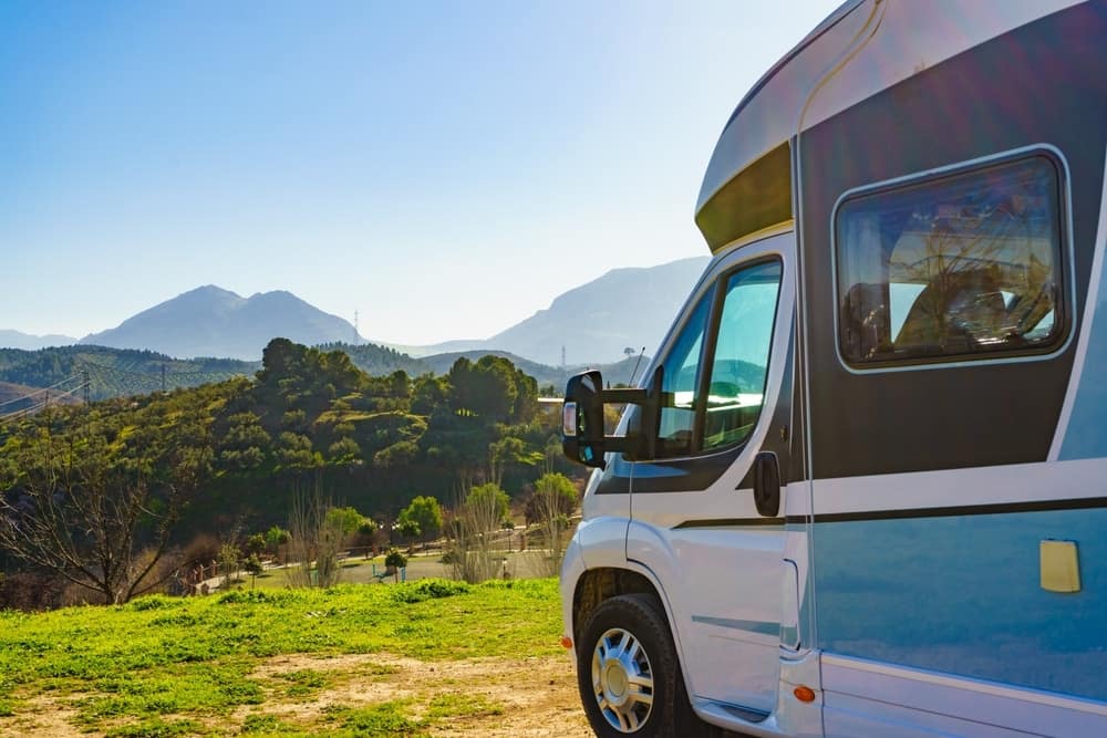 A blue and white RV parked in a field with mountains in the background, showcasing the growth of the Spanish caravanning sector.