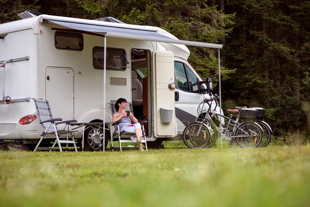 A woman sits in front of an rv with a bicycle in front of it.