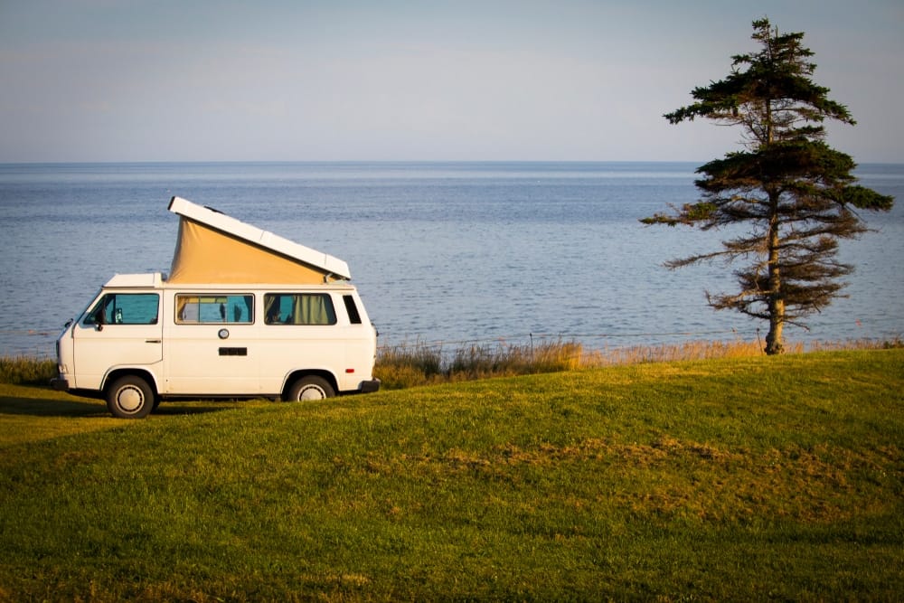 A vw camper van parked on a grassy hill next to the ocean in Prince Edward Island Campgrounds.