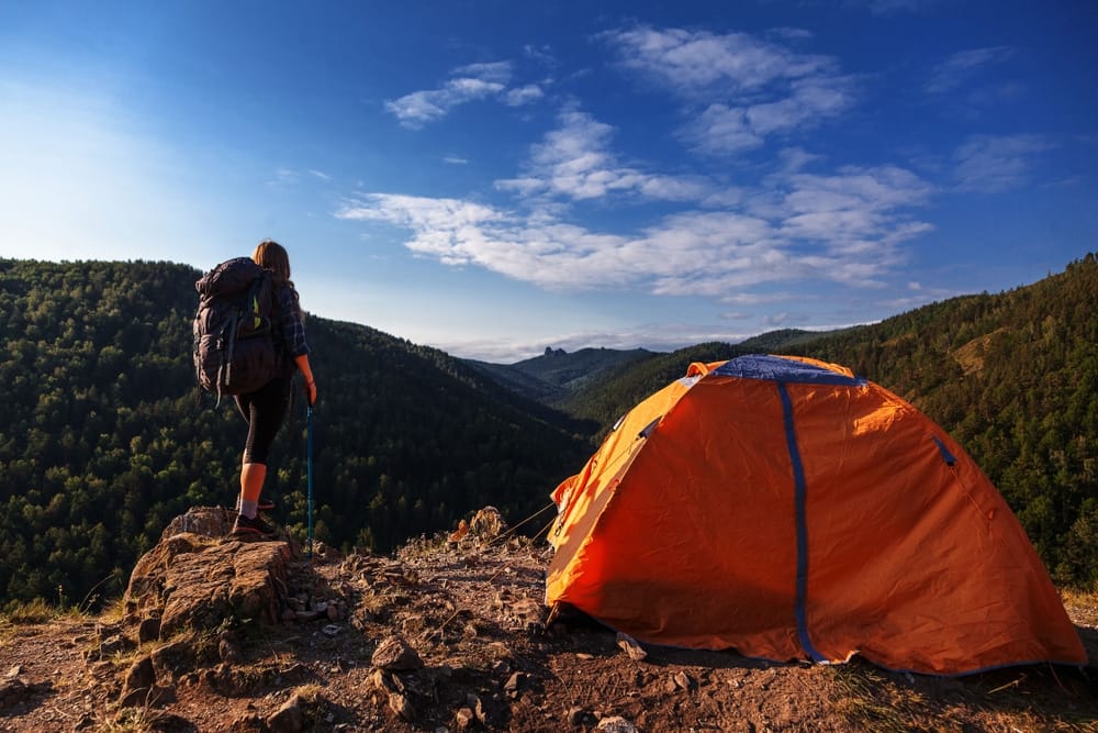 A woman is standing next to a KOA tent in the mountains.