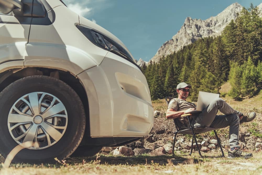 A man sitting in front of a van with a laptop, exploring virtual tours.