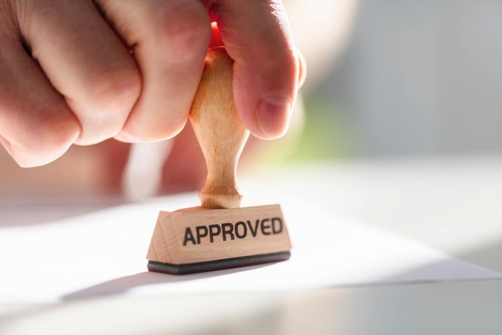 A person holding a rubber stamp with the word approved on it for KOA's Glamping Project in Wilmington.