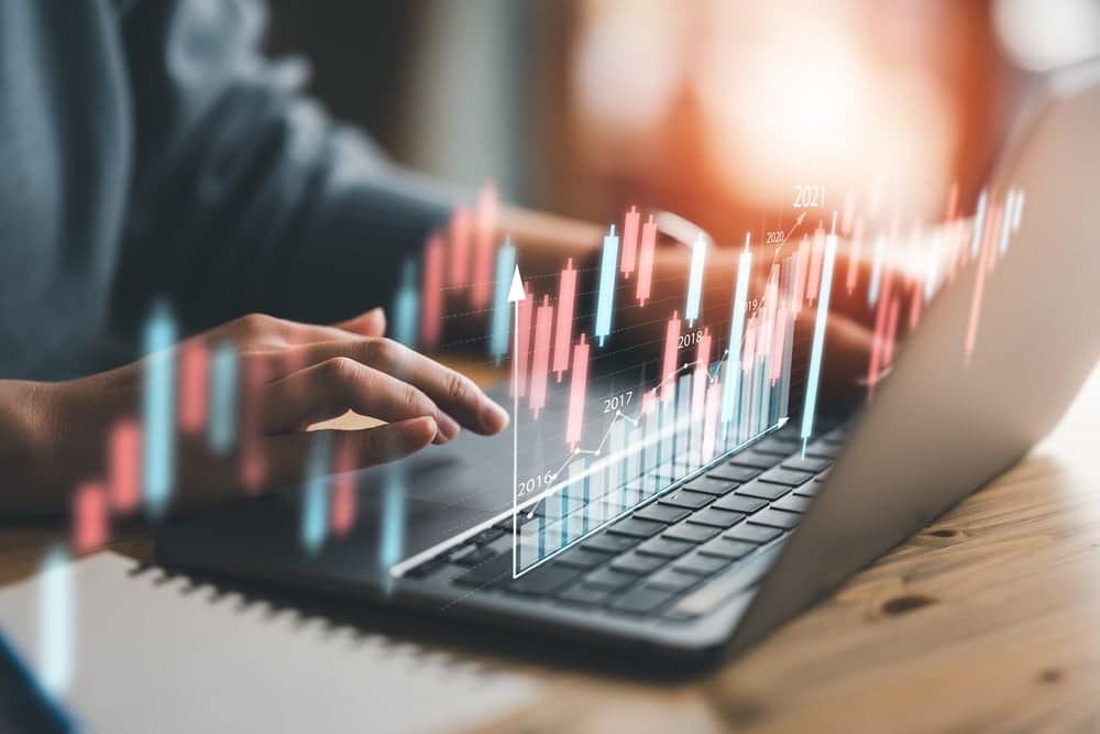 A person typing on a laptop with a stock chart showing Winnebago Industries' Q3 Fiscal 2023 results, reflecting rising industry optimism.