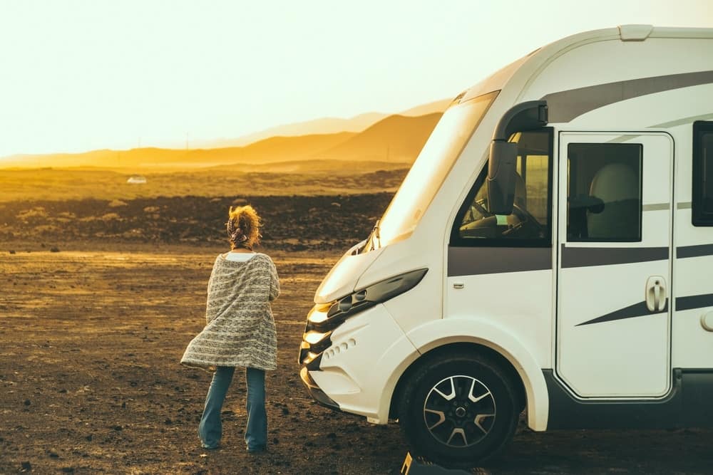 A woman standing next to an rv at sunset.