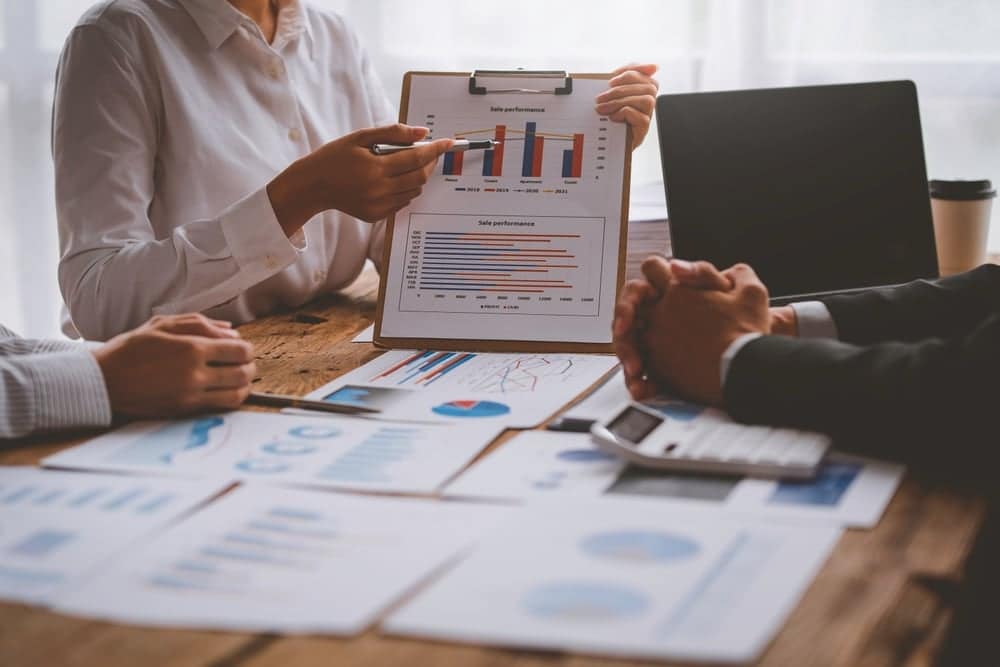 A group of business people unveils a clipboard with graphs on it, focusing on 2022 market trends.