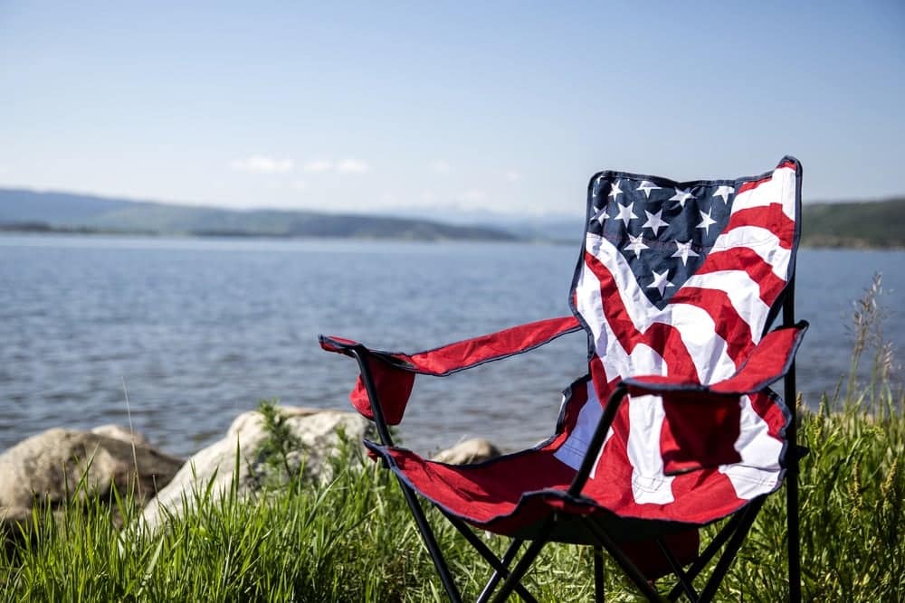 A Jellystone Park flag folding chair sits on the shore of a lake.