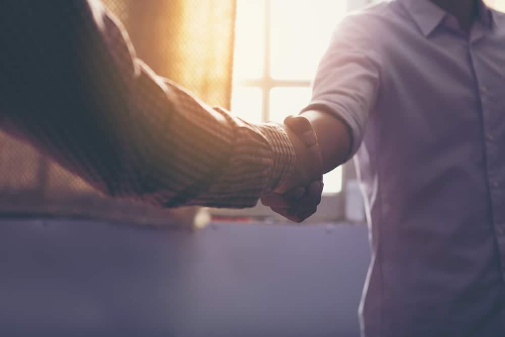 Two men shaking hands in front of a window at an RV Resort.