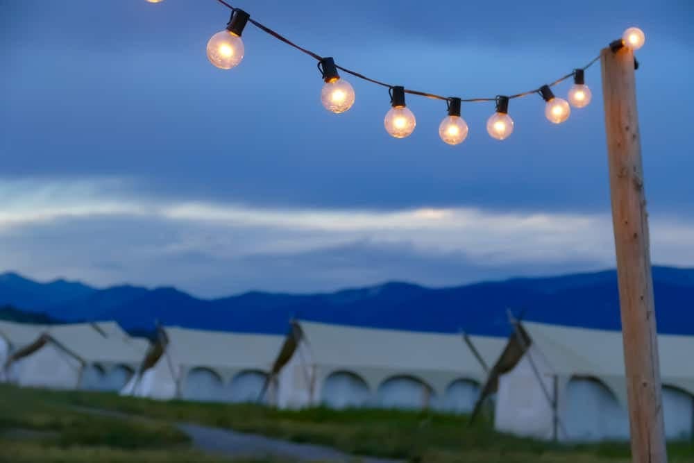 A group of tents with string lights and mountains in the background, perfect for outdoor recreation in Montana.