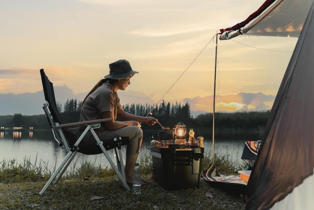 At sunset, a woman sits in front of a tent, creating an idyllic scene for outdoor recreation.