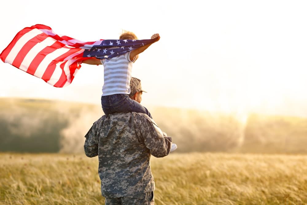 A military member is holding an American flag over his head.