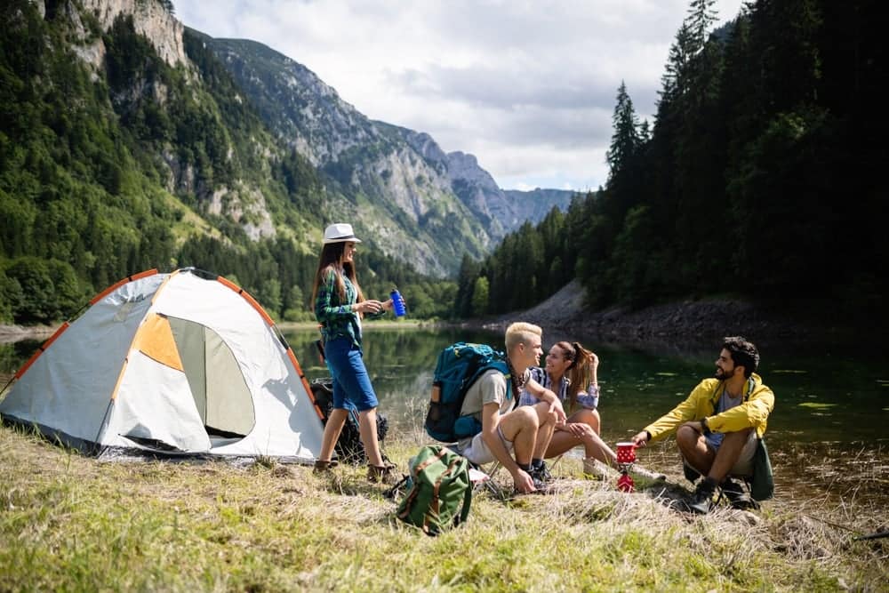A successful camping business team sitting around a tent near a lake.