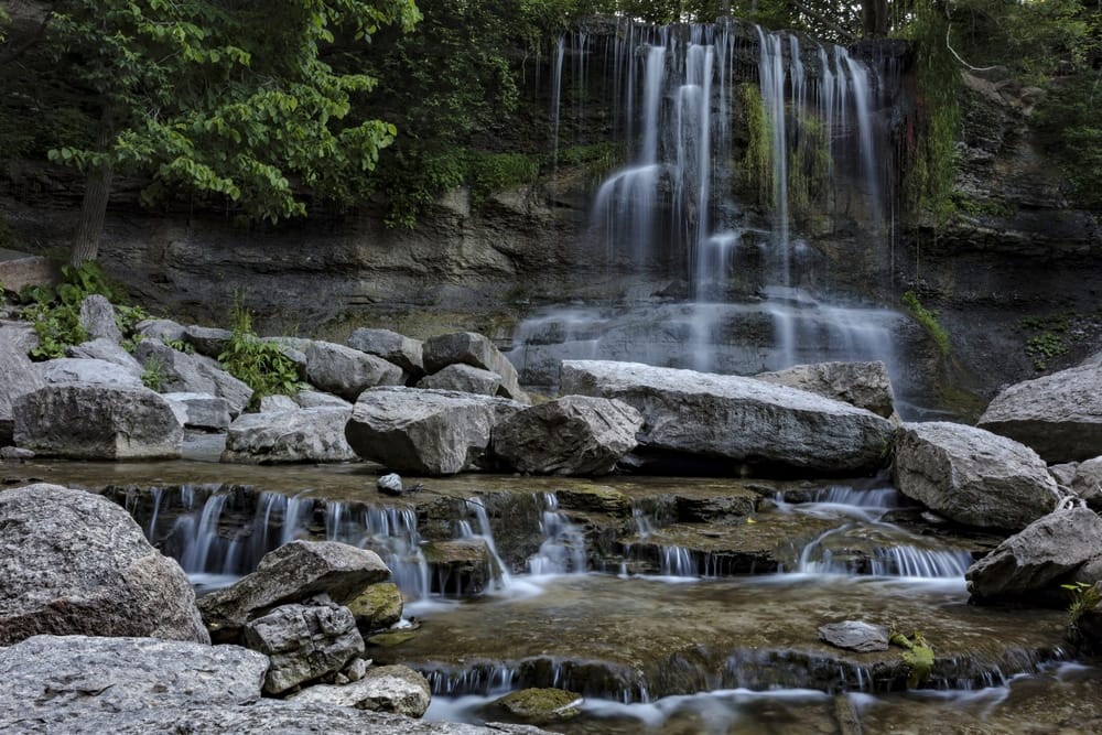 A picturesque waterfall nestled among the serene beauty of rocks and trees in Lambton County's Conservation Area.