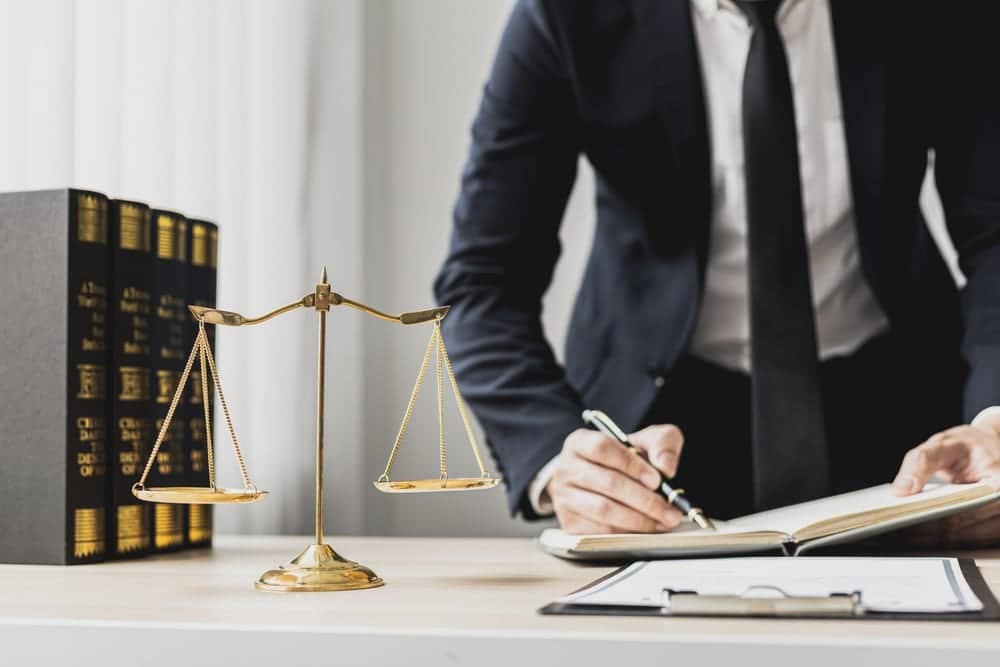 A man in a suit is writing on a scale of justice during a lawsuit involving the WACO campground ordinance revision.