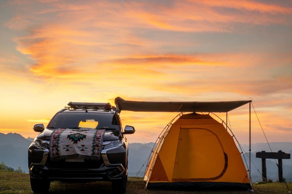 An extended SUV with a pop-up camping tent next to it at sunset.