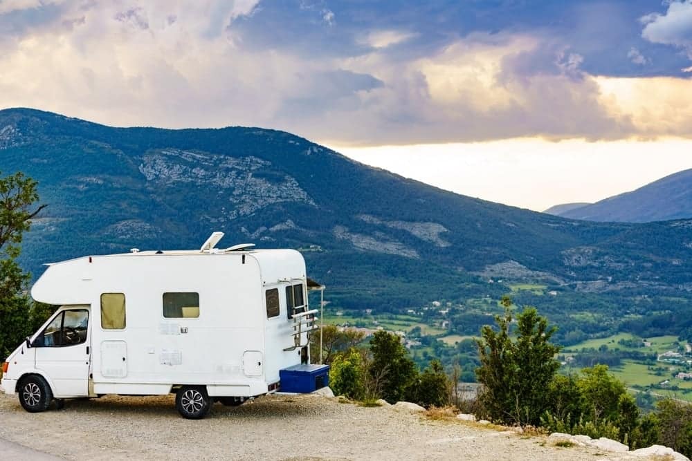 A European caravan parked on the side of a road, surrounded by majestic mountains.