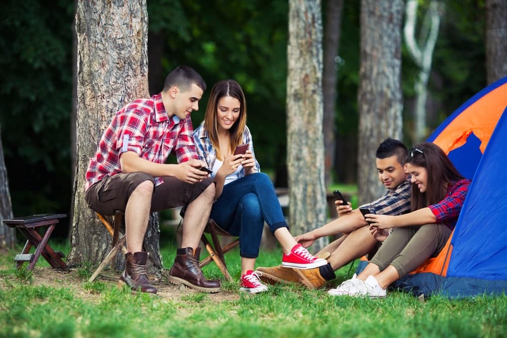 A group of young people enjoying outdoor entertainment in front of a tent, using their cell phones.