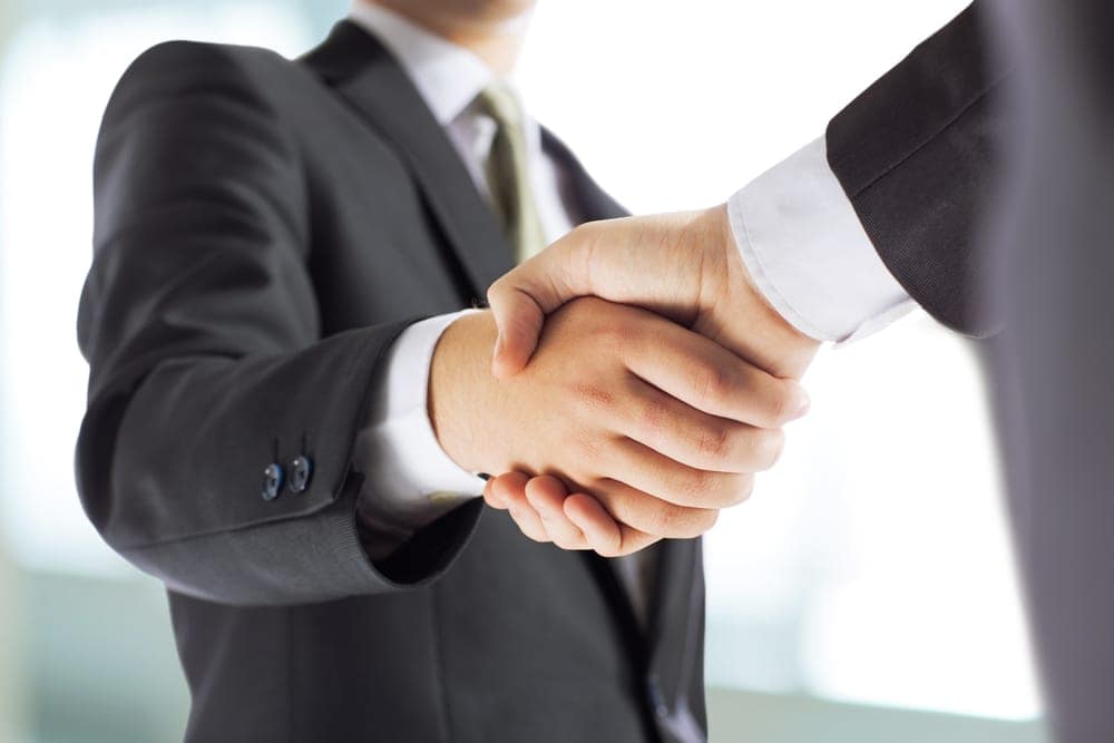John Burke, KOA CFO, shaking hands with a representative from KCN Campgrounds in front of an office.
