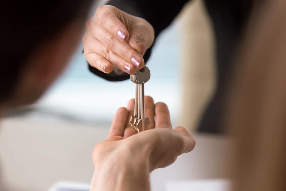 A woman confidently handing a person the key to a house, ensuring their security and accommodations.