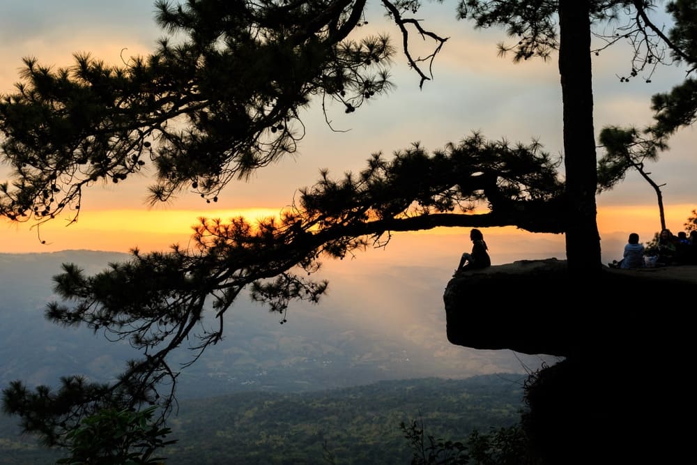Adventurous exploration at Phu Kradueng National Park, where people sit on top of a cliff watching the sunset.