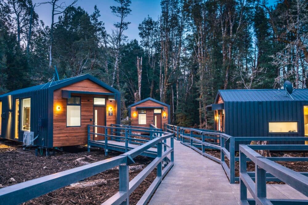 Transforming wilderness luxury at Discovery Parks - Cradle Mountain, featuring tiny cabins in the woods at dusk.