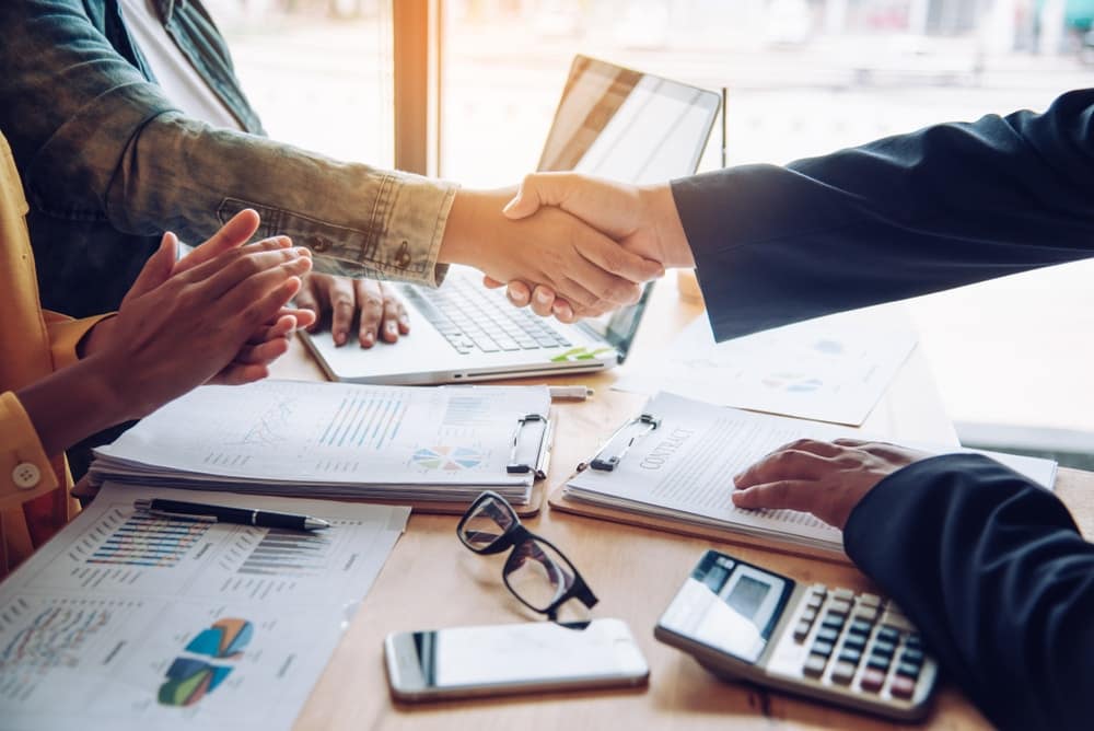 Two business people shaking hands at a desk during an ELS acquisition.