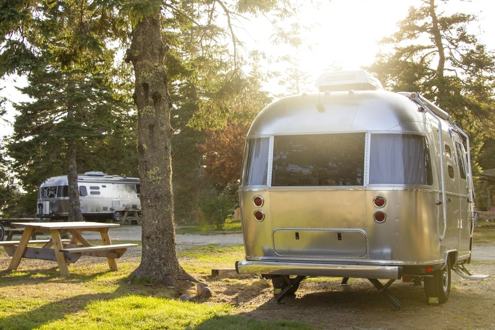 A silver airstream, perfect for RVing adventures, parked in a serene wooded area.