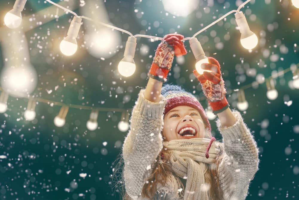 A girl is holding a string of lights in the snow.