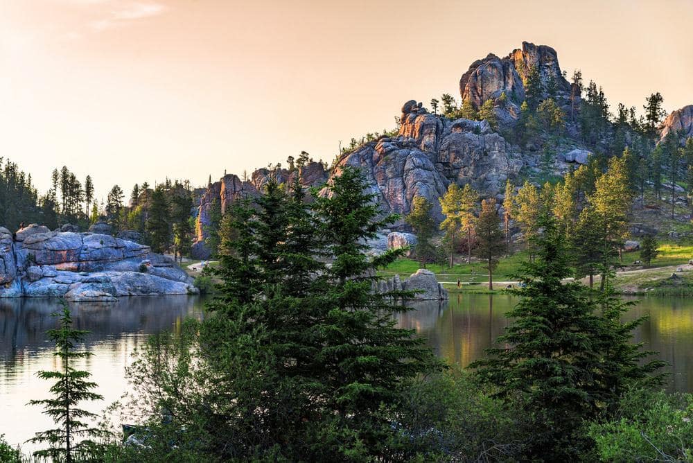 A serene lake nestled in the midst of towering trees and rugged rocks, offering a perfect retreat for Black Hills vacations.