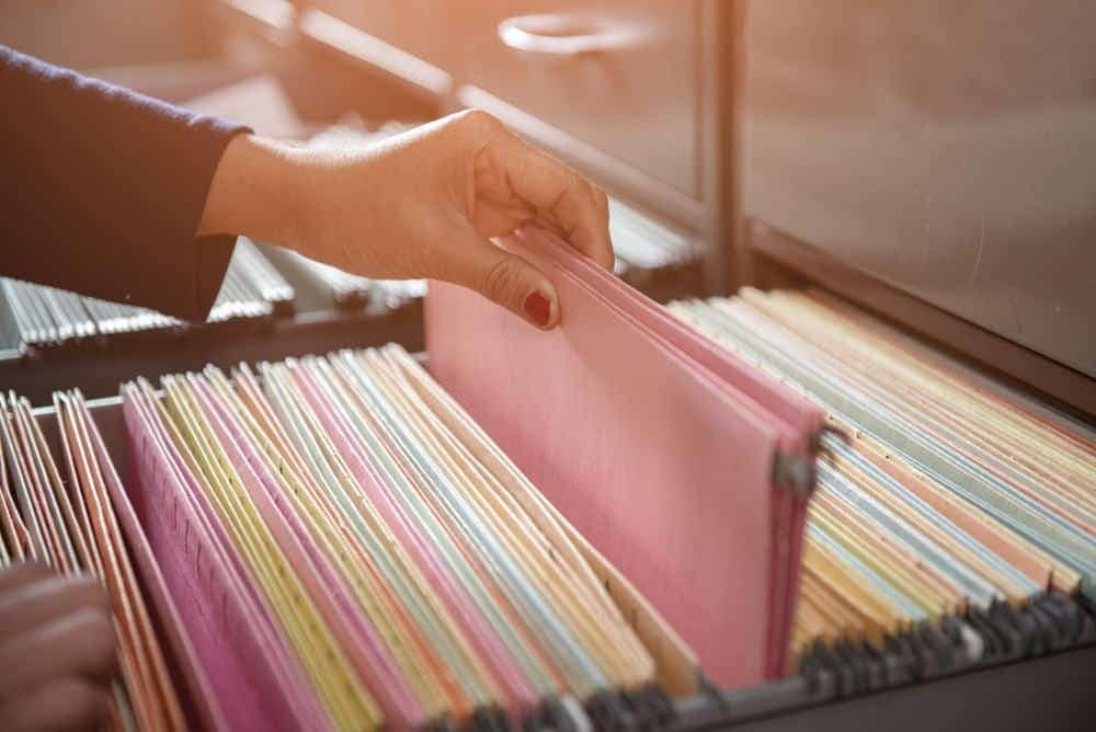 A person opening a file folder in a filing cabinet.