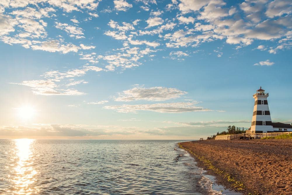 A Prince Edward Island lighthouse sits on a sandy beach at sunset.
