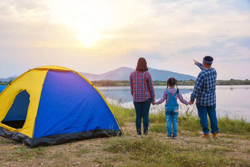 A household is standing next to a tent in front of a lake, enjoying the outdoors.