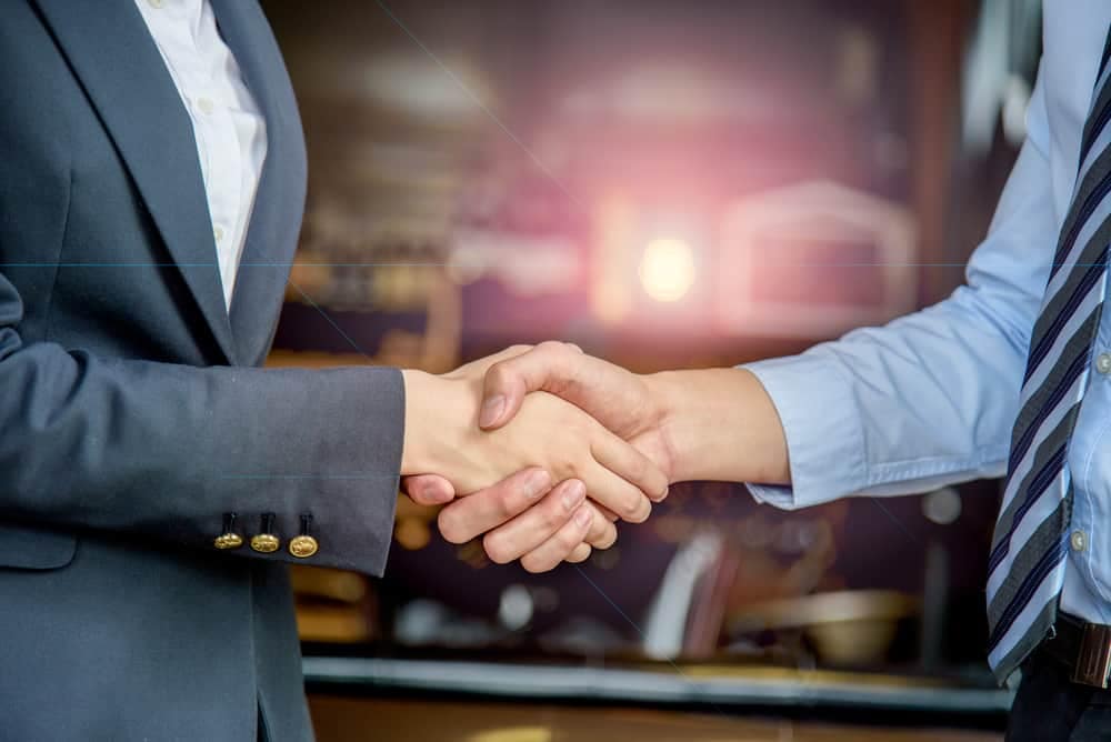 Two business people from DexKo Global and Premium Supply Ltd shaking hands in front of a bar.