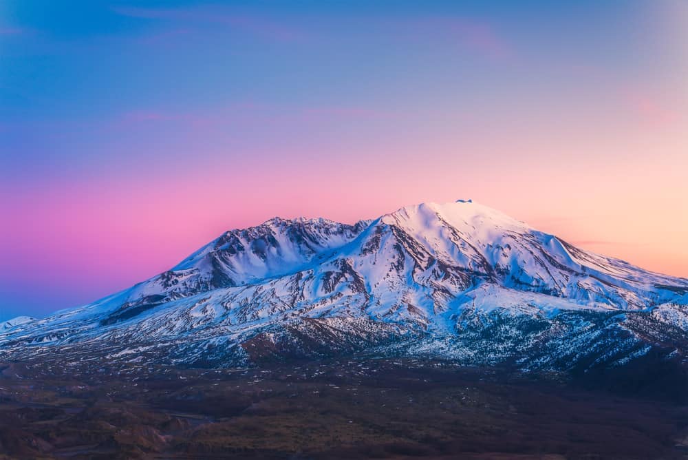 Mount St. Helens, a majestic mountain covered in snow, emerges against the backdrop of a captivating pink and purple sky at the National Monument.