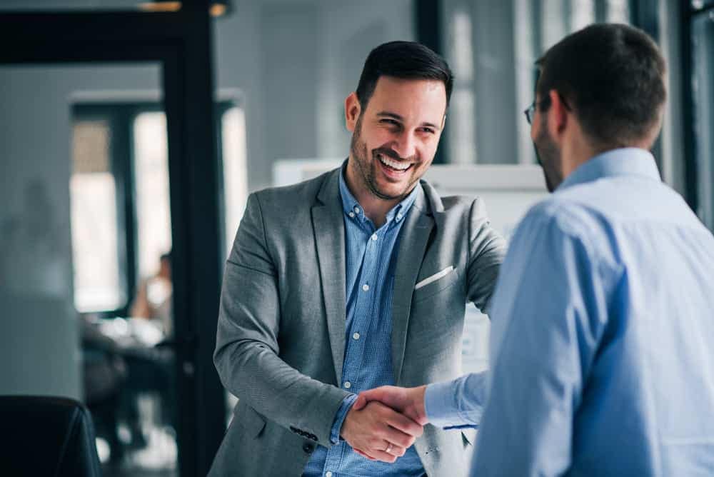 Two businessmen, one from Bailey of Bristol and the other a Ford Qualified Vehicle Modifier, shaking hands in an office.
