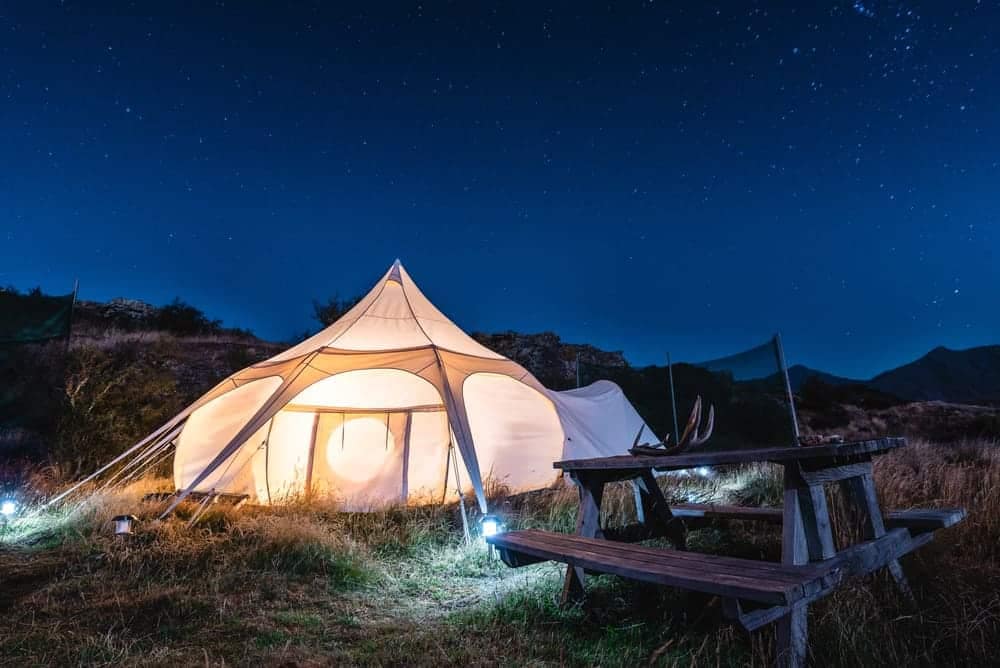 A glamping tent lit up at night with a picnic table.