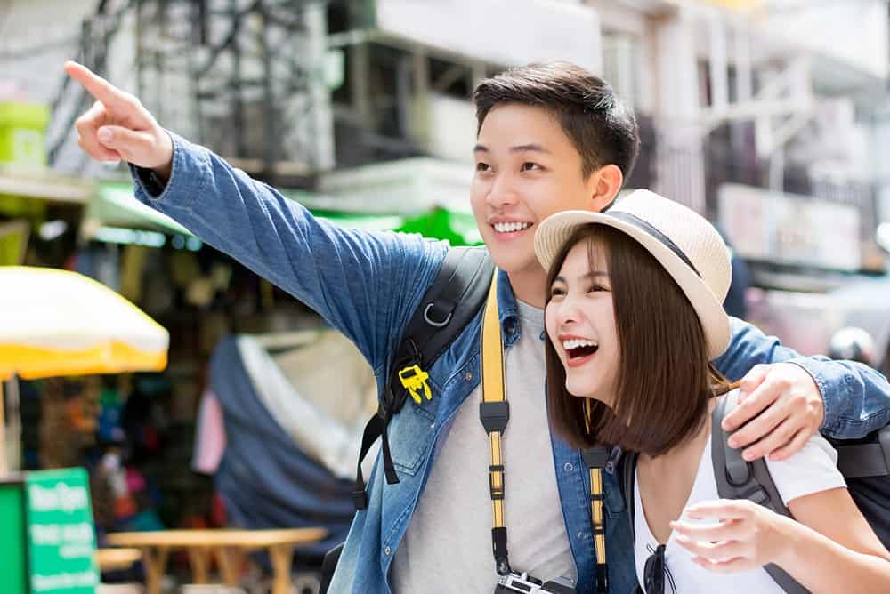 Two Chinese tourists pointing at something in the street while discussing their travel plans.