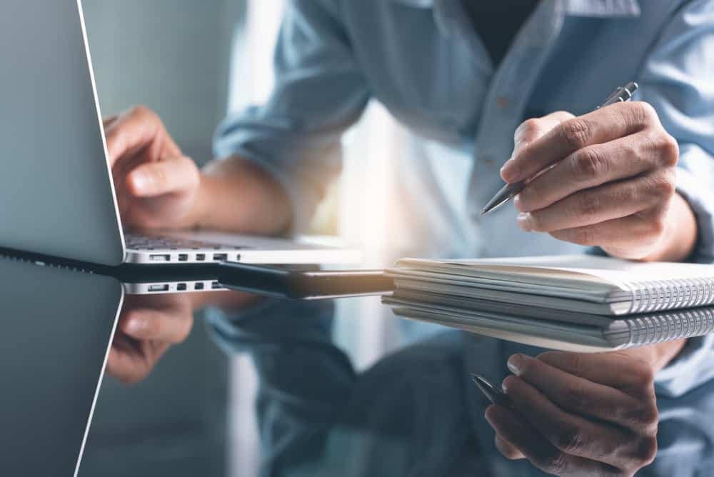 A person working on a laptop with a pen, avoiding common pitfalls while mastering the RV Destination Mastery Course for prospective owners.