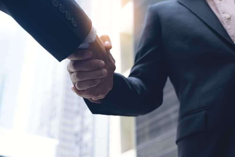 Two businessmen, representing Findlay RV and Lazydays respectively, shaking hands in front of a building to celebrate the announcement of their acquisition agreement.