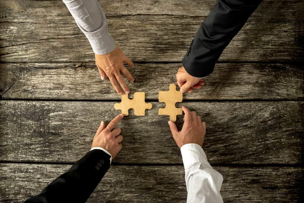 Go Auto expands footprint with Bellingham Dealerships as three business people holding puzzle pieces together on a wooden table.