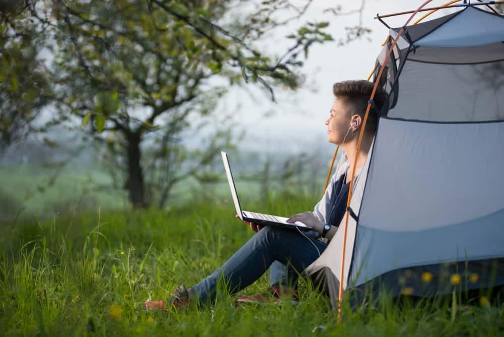 A man sitting in front of a tent with a laptop enjoying Wi-Fi services in Manitoba.