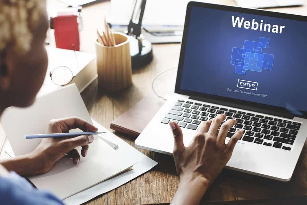 A woman is diligently working on her laptop, specifically engrossed in a webinar that prominently displays the word "webinar" on its screen.