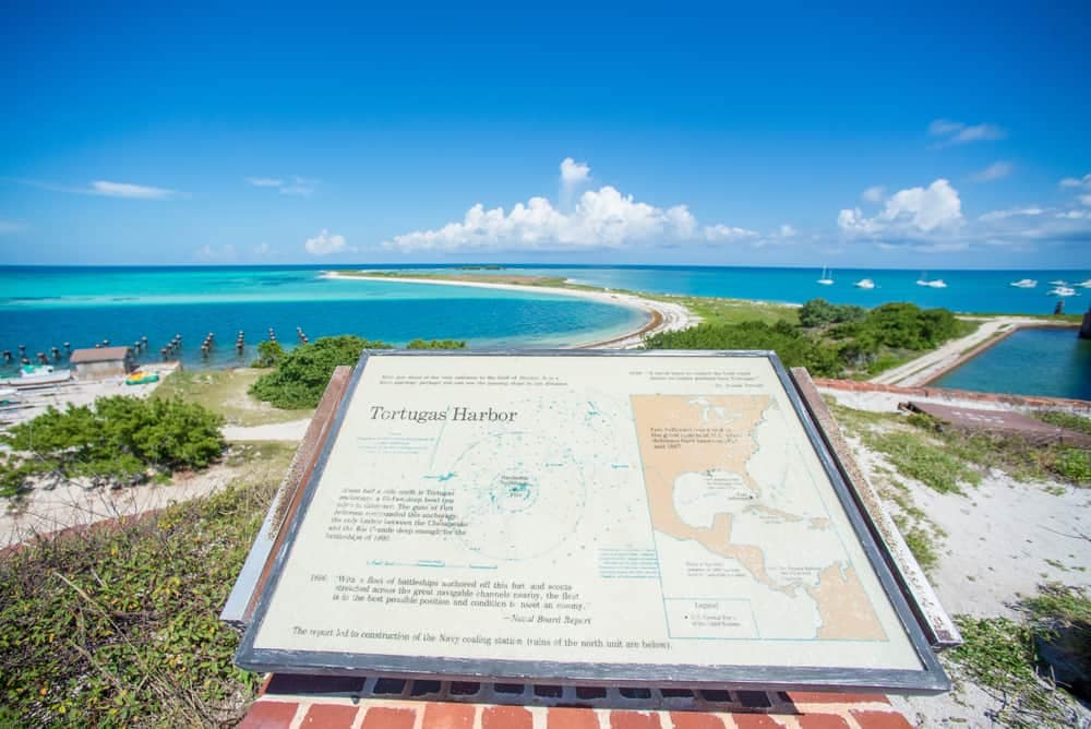 A sign on a hill overlooking a beach and ocean, guiding campers to explore nearby public land areas using Hipcamp.