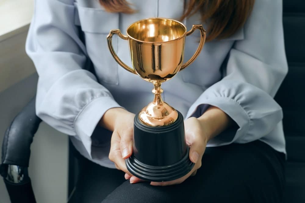 A woman holding a gold trophy in an office chair, representing her success as a leading franchise owner in the recession-proof KOA franchise.