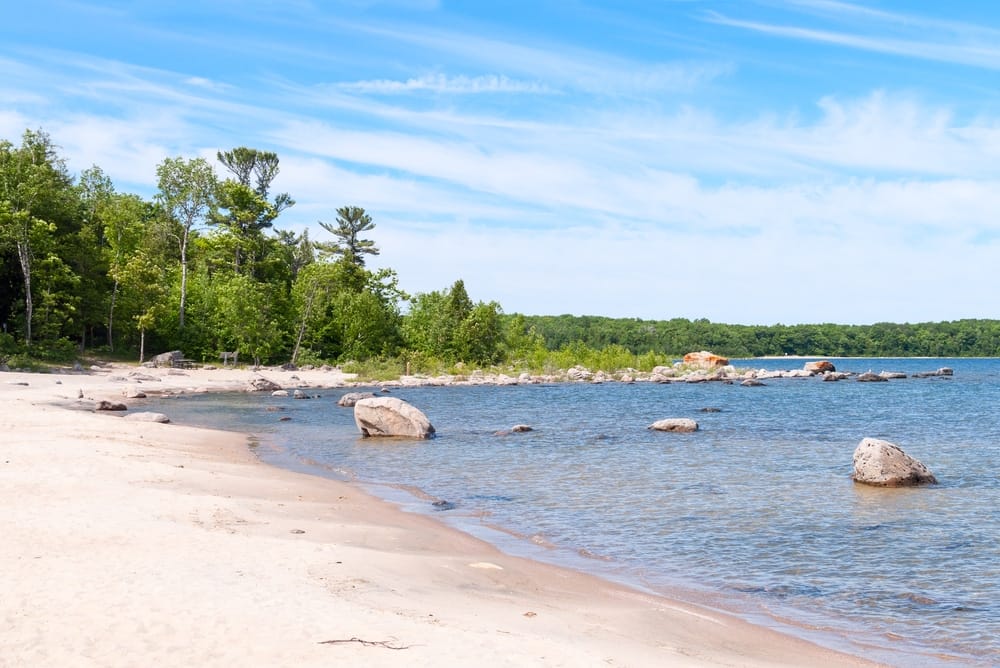 Awenda Provincial Park, located in Ontario and managed by the Ontario Gov't, offers a picturesque sandy beach along the shoreline, featuring stunning views of the body of water.