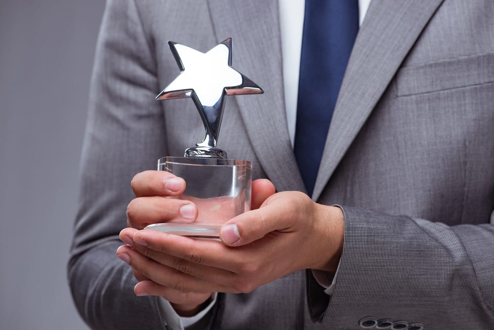 A businessman proudly holding an award with a star on it, representing his recognition as the Best Employer in the Manufacturing industry at Grand Design RV.