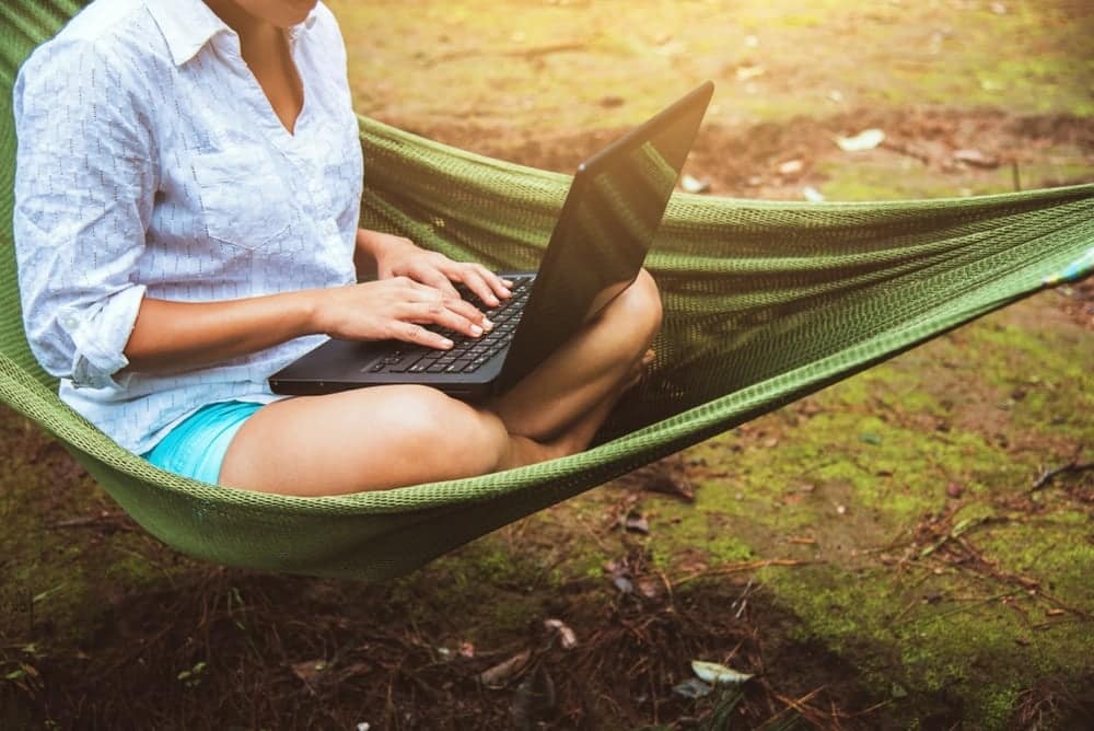 A woman is sitting in a hammock using her laptop while enjoying the peaceful surroundings provided by Good Sam.