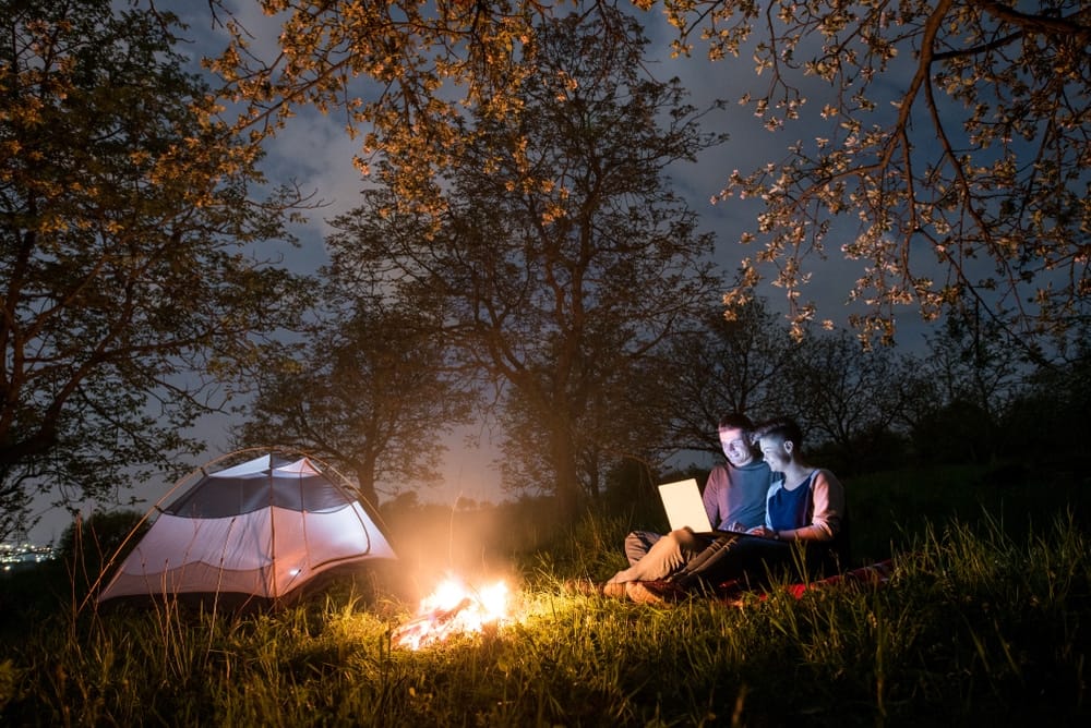 A couple sitting at an RV Park campfire in Texas, engrossed in a laptop for the Tech Upgrade Contest.