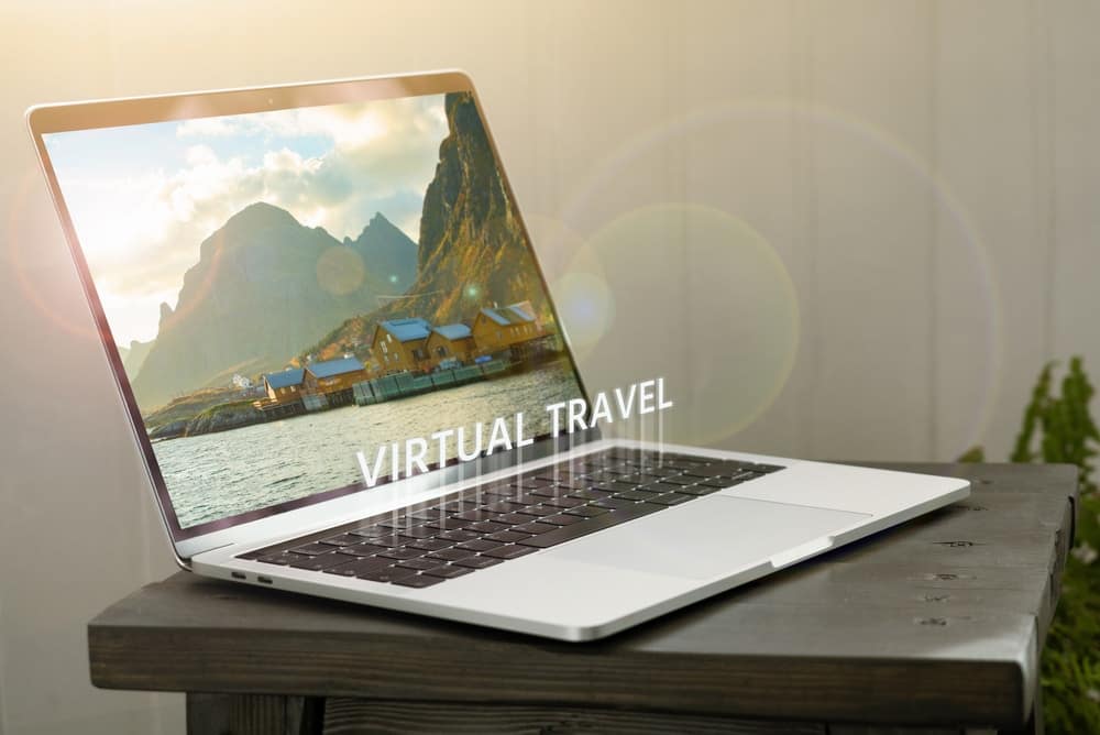 A laptop displaying the word virtual travel on its screen, placed on a wooden table.