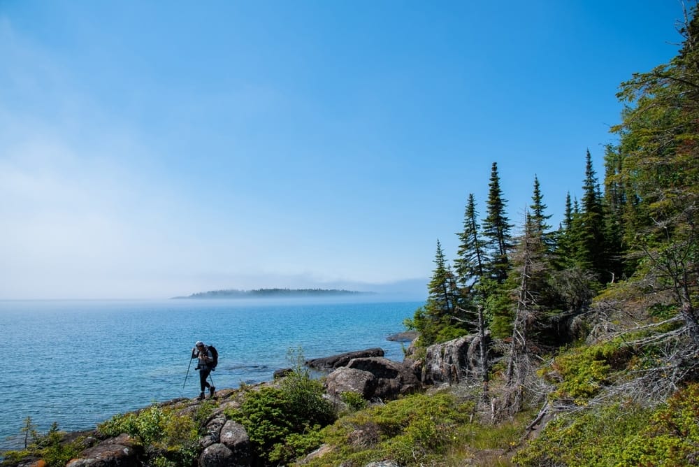 A hiker standing on a rocky cliff overlooking the water in Isle Royale.