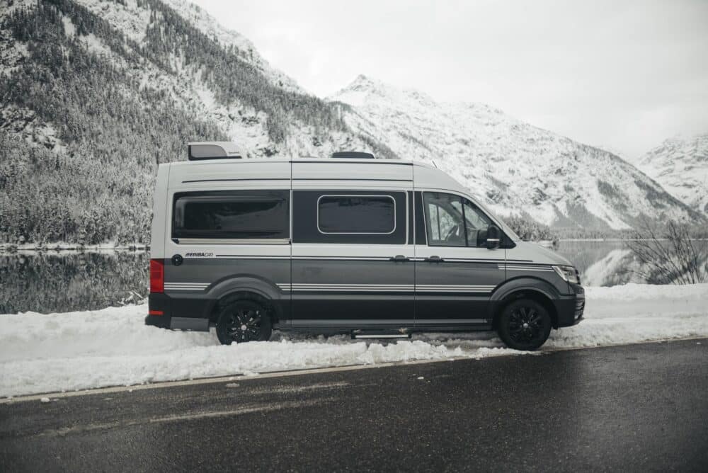 An Eriba Car Camper Van parked in the snow near a lake, attracting younger travelers.